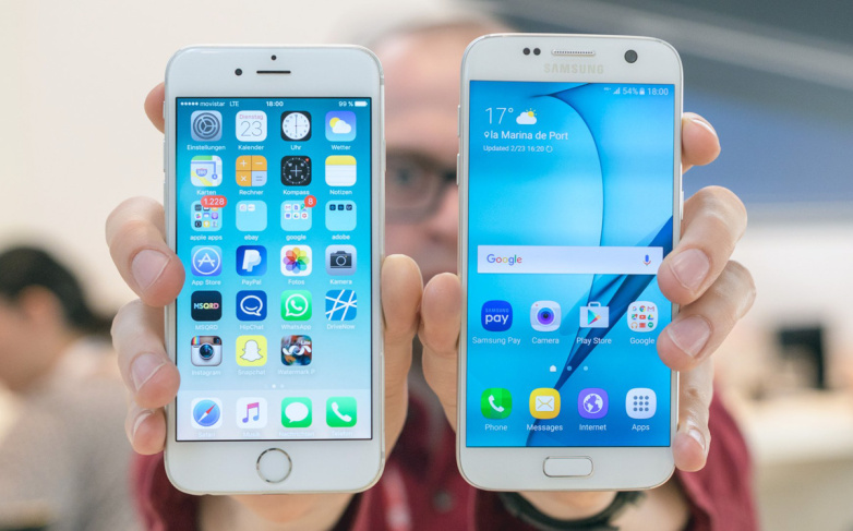 Image description: A blurred out man holdiing out two white mobile/cell phones, one Apple, one Android