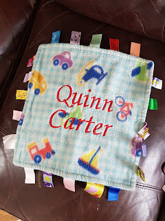 An image of a colourful square of material with lots of tags protruding from the edges and the name ‘Quinn Carter’ written on it in red