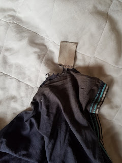 An image of a dark blue, slightly ripped T-Shirt with a grey Tag sticking out, on a white background